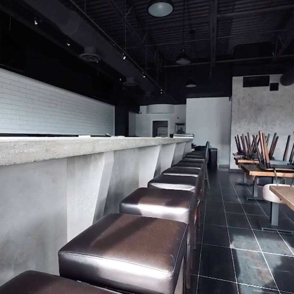 Iron Shake Inc Empty restaurant interior with a row of barstools along a counter and chairs stacked on tables, featuring dark flooring and high ceilings—a showcase of Iron Shake Inc's expertise in commercial construction services. Commercial Contractor
