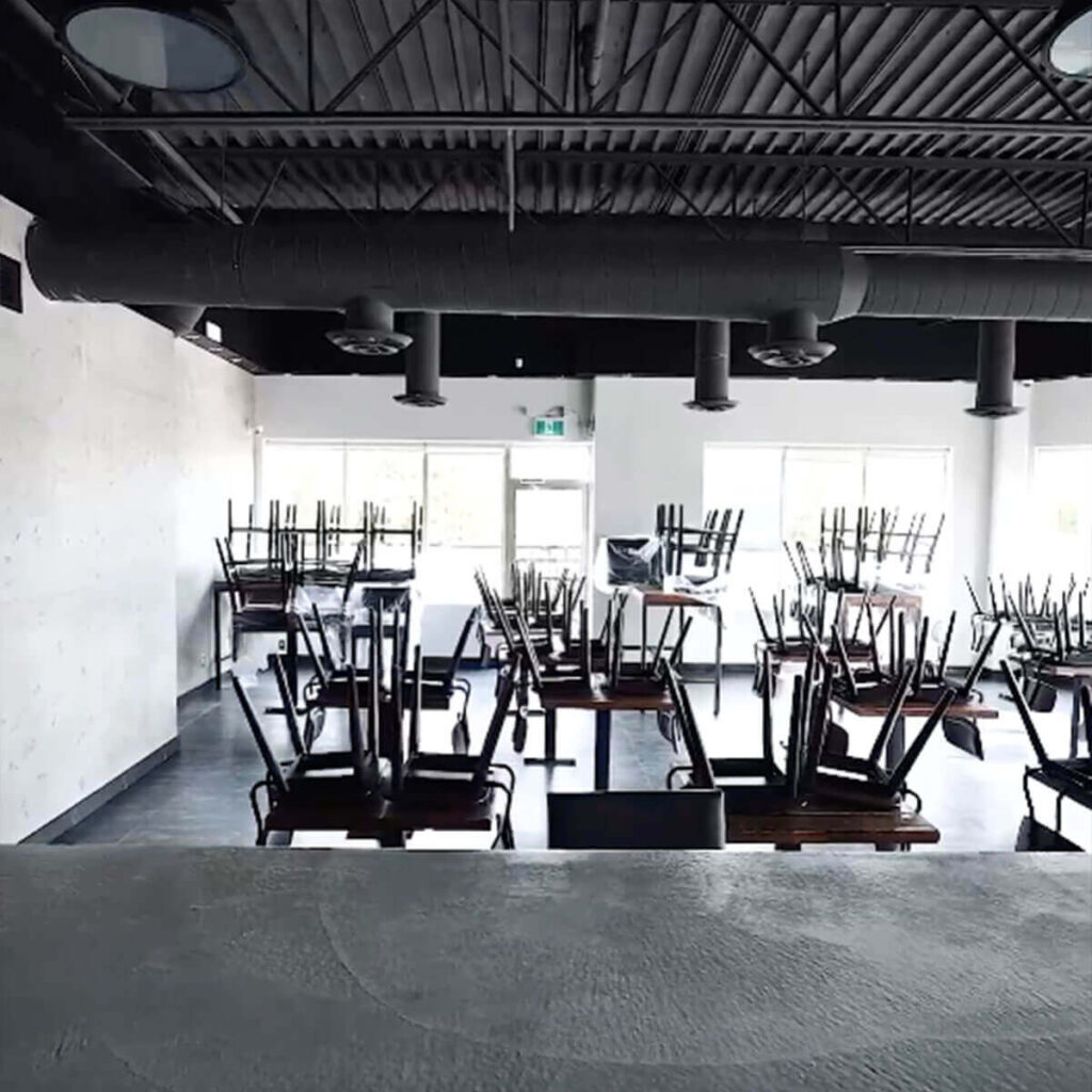 Iron Shake Inc Empty restaurant interior with chairs stacked upside down on tables, seen from behind a counter, with large windows letting in daylight—a testament to quality commercial construction services by Iron Shake Inc. Commercial Contractor