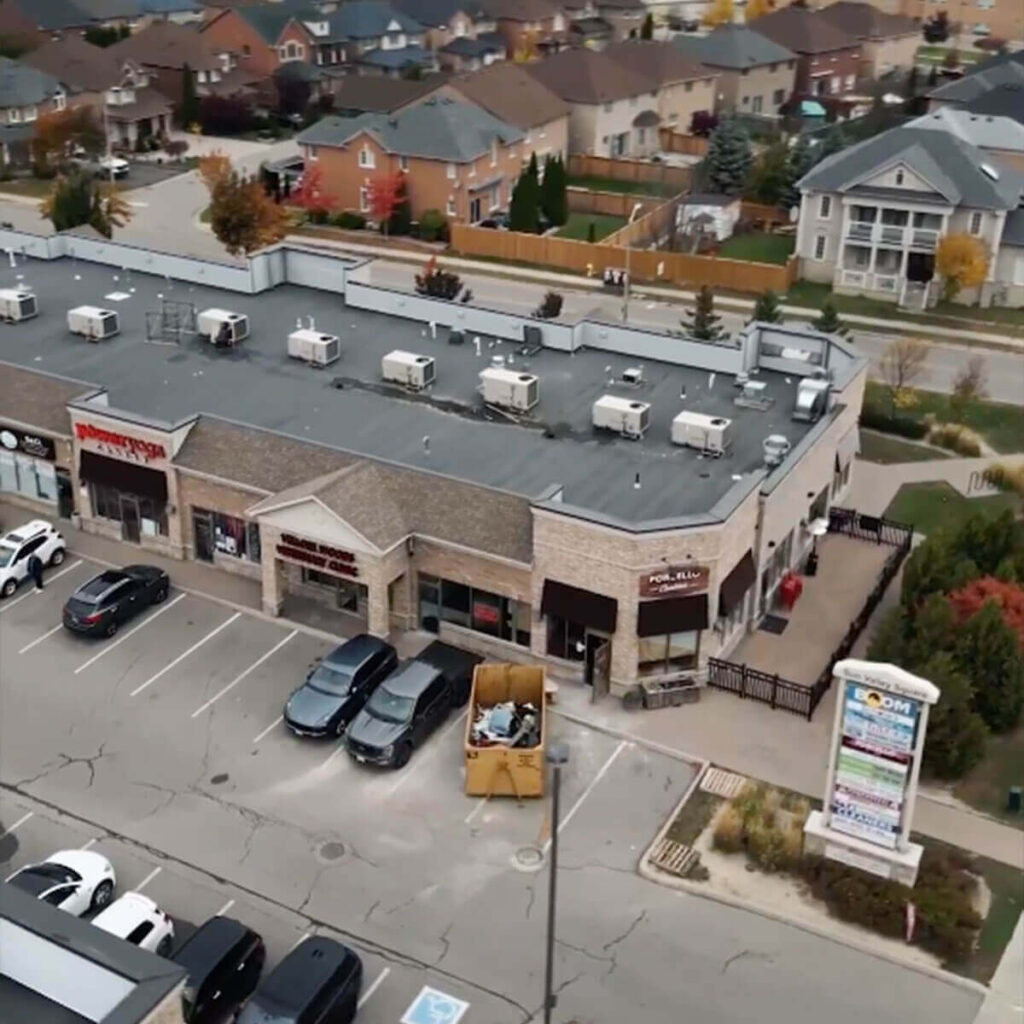 Iron Shake Inc Aerial view of a small shopping plaza with several businesses—built by Iron Shake Inc, experts in commercial construction services—parked cars in front, and residential houses in the background. Commercial Contractor