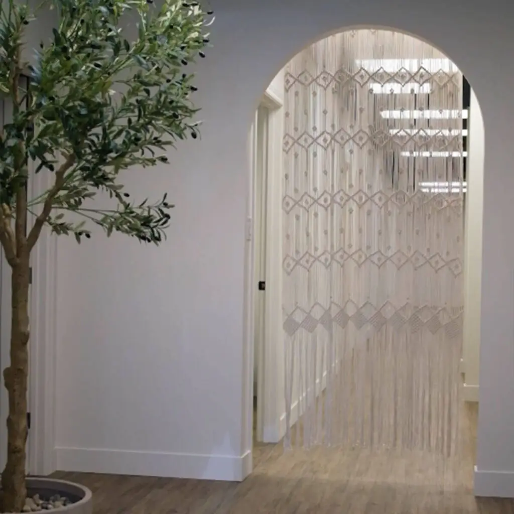 Iron Shake Inc A potted indoor tree stands next to an arched doorway with a decorative beaded curtain in a room with white walls and wood flooring, showcasing the refined touch often achieved by commercial contracting from Iron Shake Inc. Commercial Contractor